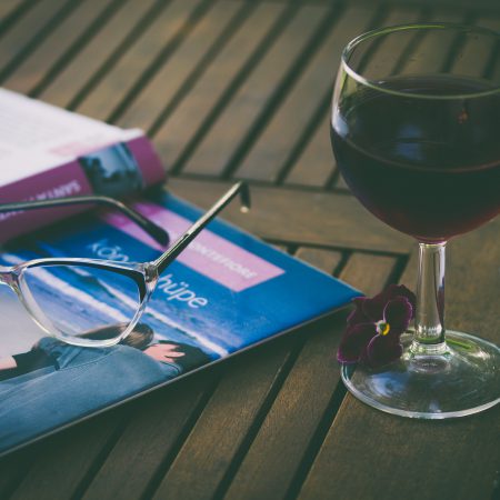 A glass of wine sits next to a book and a pair of glasses